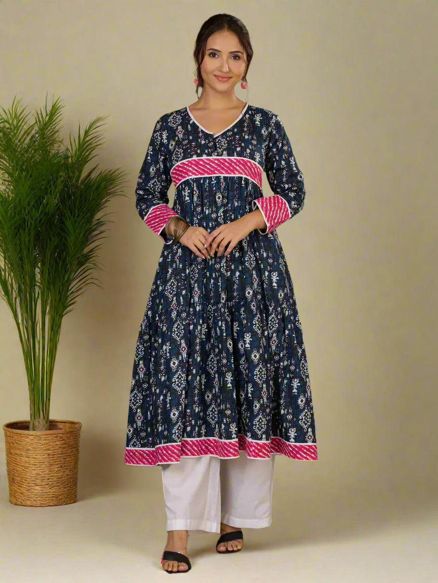 Woman wearing a navy blue kurta with pink accents standing next to a plant on a green background
